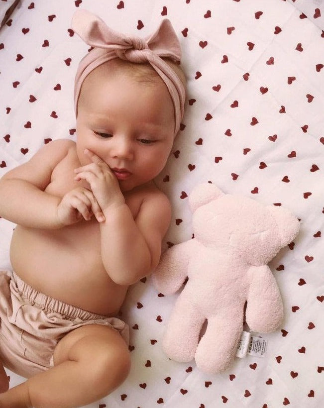 Baby lying down with headband on and teddy 